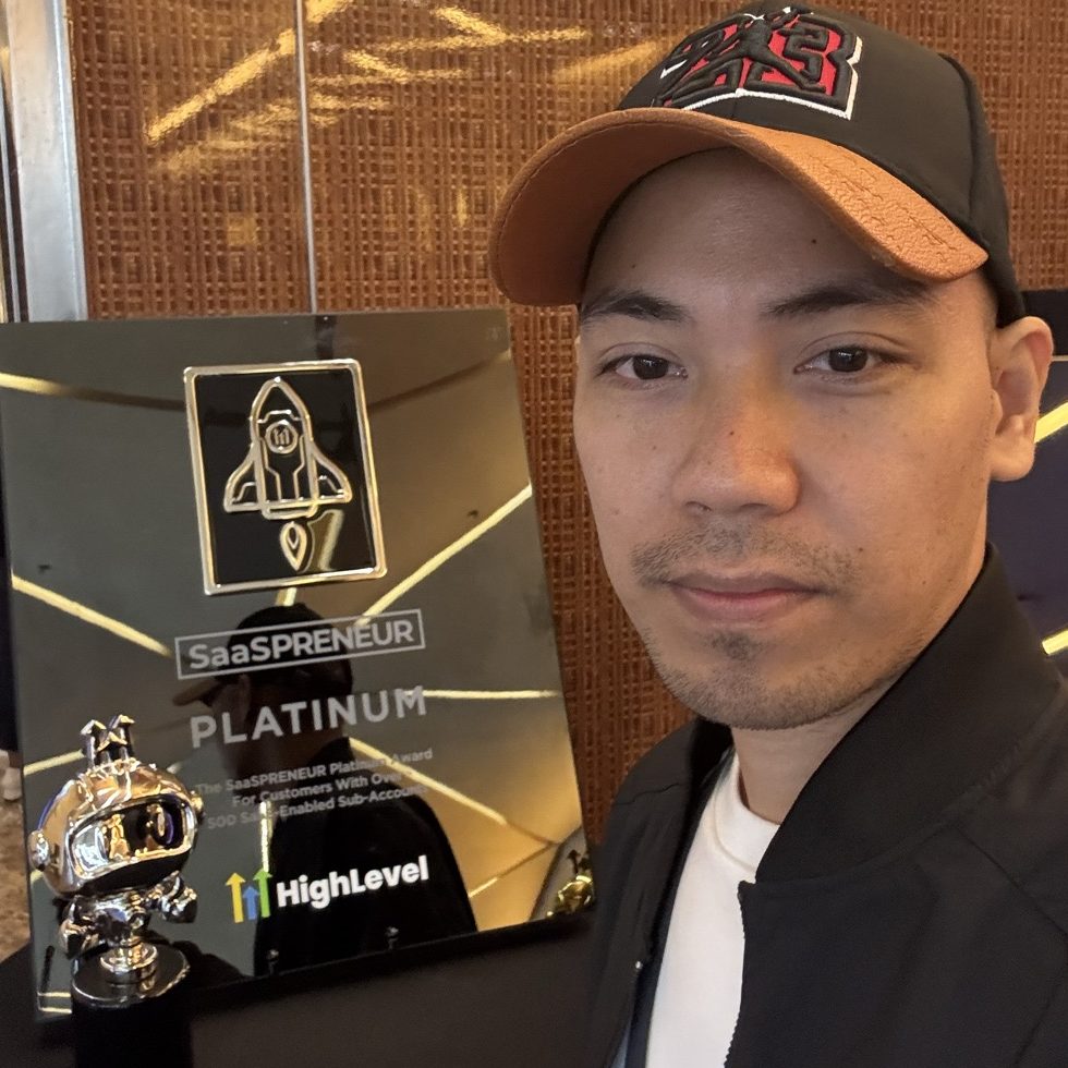 Kevin Ordoñez beside a HighLevel SaaSPRENEUR Platinum award plaque and a chrome astronaut trophy at a HighLevel event.